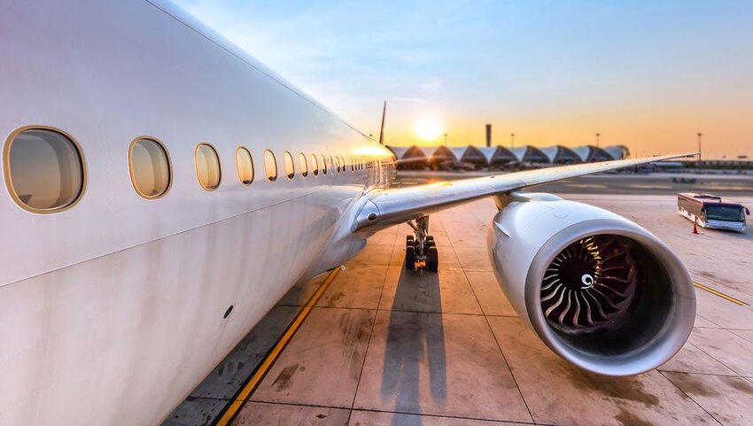 Side of plane, wing, and engine at sunset.