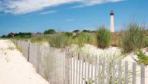 Sand dunes and fence with house and the Cape May lighthouse in the distance. 