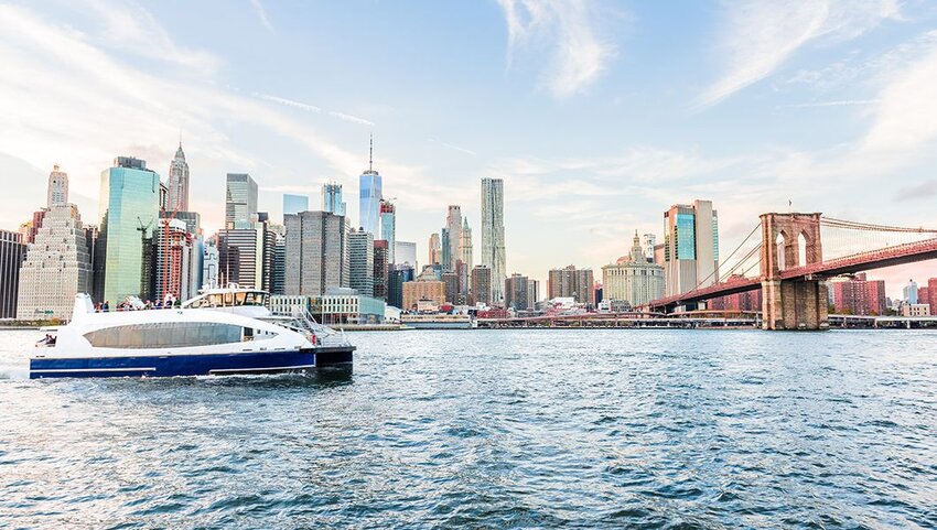 Ferry riding by New York City skyline and Brooklyn Bridge.