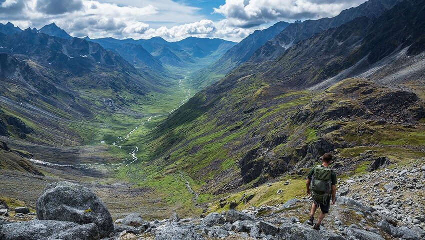 A man walks down a steep trail above a glacial valley in the Talkeetna Mountains.