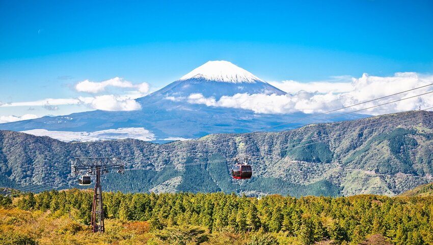 Aerial tram over trees with Mount Fuji in distance.