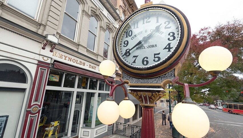 Decorative clock on street in front of storefront.