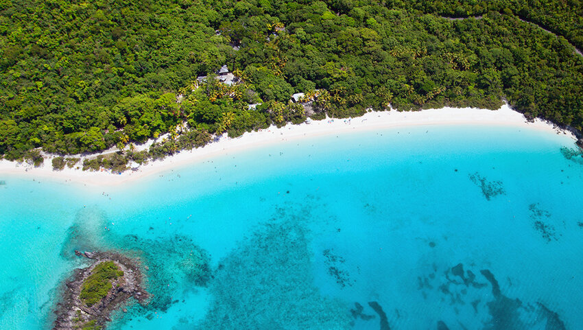 Aerial of Trunk Bay, with water, beach, and tree covered landscape. 