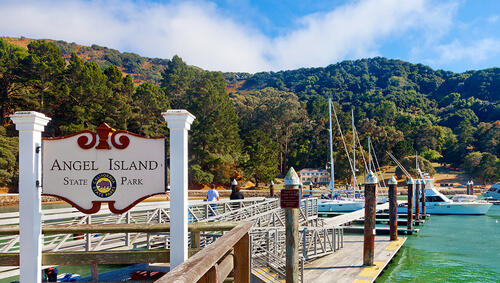 Sign for Angel Island State Park in dock  with boats and trees. 