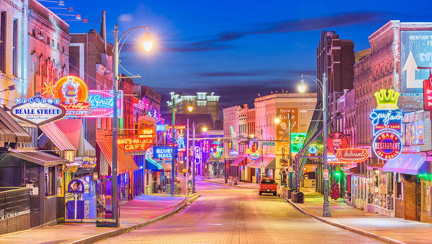 View down Beale Street at dawn, with glowing neon signs for blues clubs.