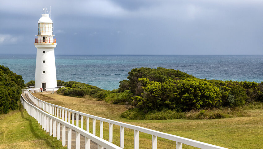 Fenced walkway to Cap Otway Lighthouse with water in background.