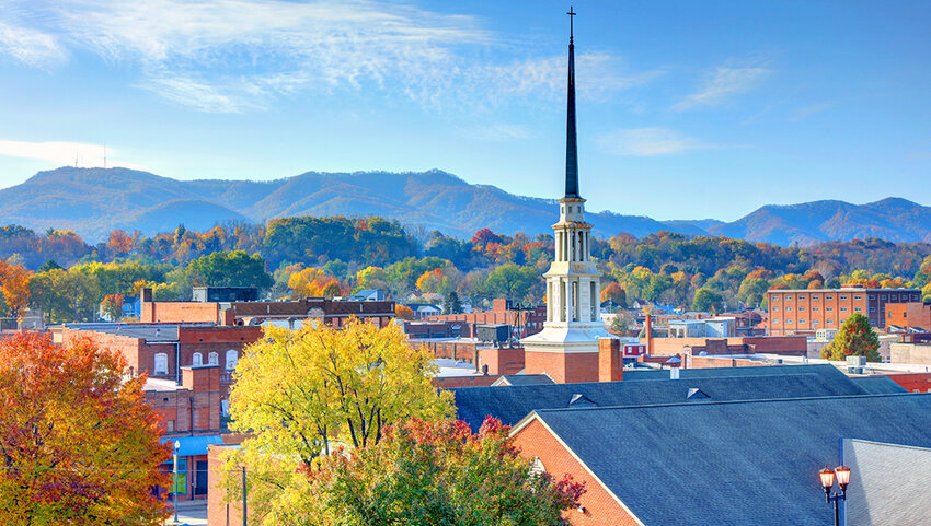 Tops of buildings, steeple of a church, fall trees and mountains in distance.