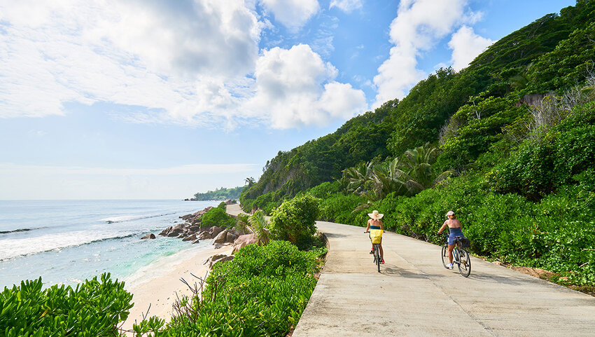 Two bike riders on paved path along beach.