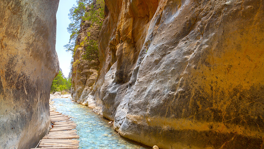 Log walkway over water through narrow trail through cliffs.