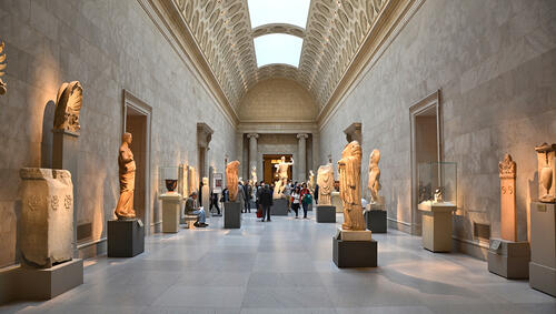 People in a long hallway gallery of Greek sculptures at The Met. 