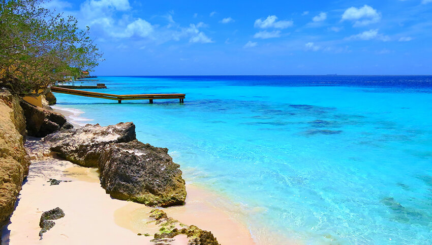Tropical white fine sandy empty beach with big stones and wooden pier.