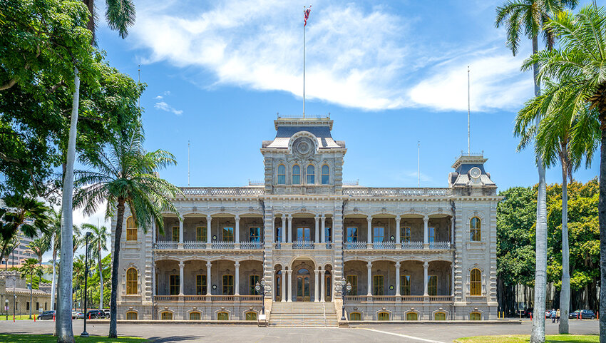 Exterior of Iolani Palace with surrounding palm trees. 