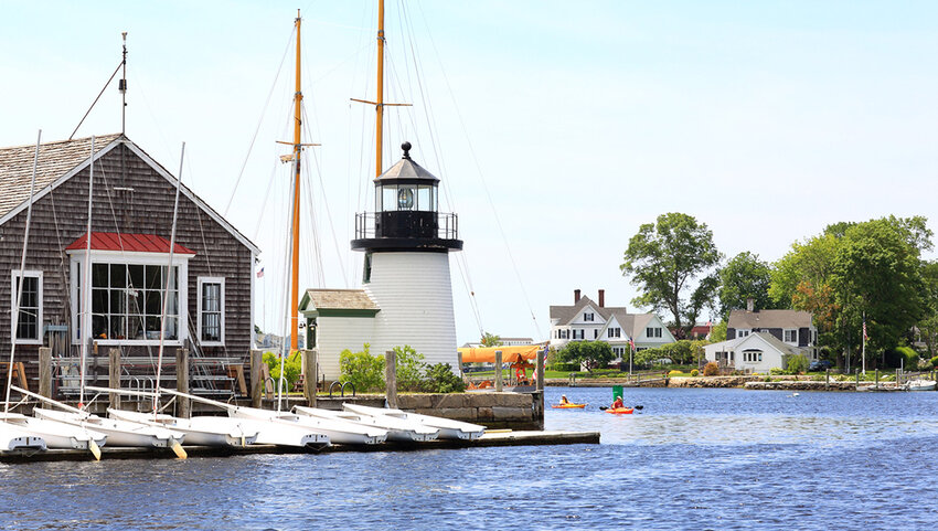 Mystic seaport with docked sailboats, buildings and kayakers.