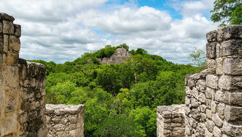 Calakmul ruins above the trees viewed through stone walls.