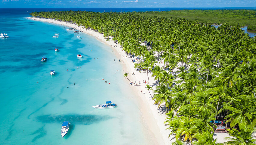 Aerial of Caribbean Sea with boats in clear blue water, beach and green palms.