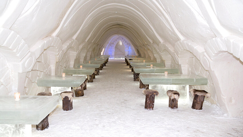 Dining room in the ice hotel, with tables made of ice and wooden stools.