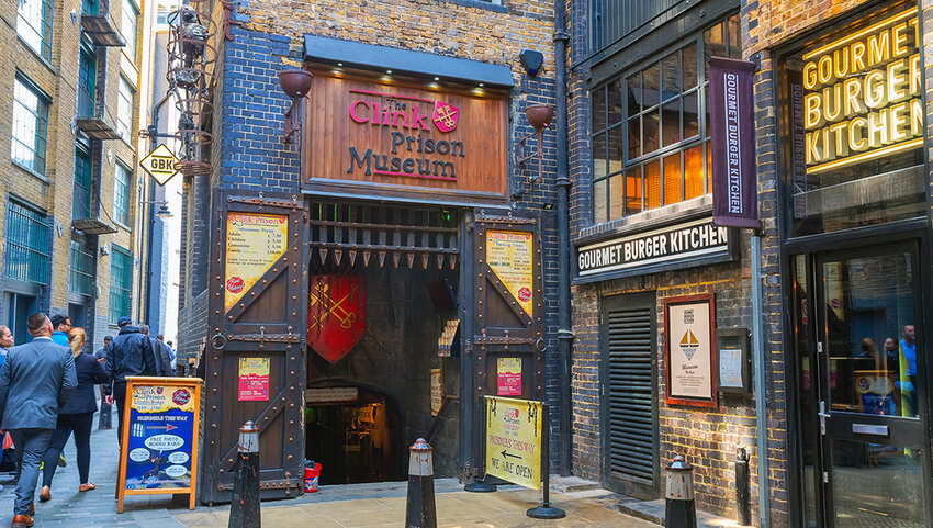 Exterior of the Clink Prison Museum entrance and surrounding businesses, with people walking on street.