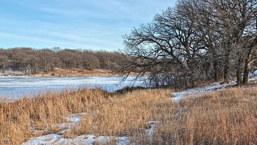 snowy landscape next to frozen lake. 