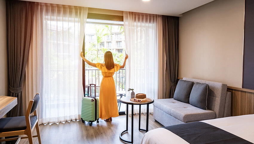Woman opening curtains in hotel room.