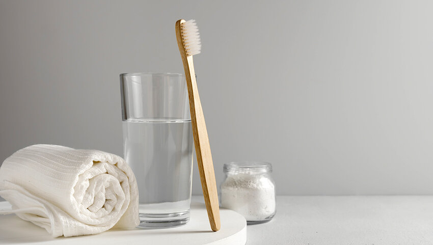 Bamboo toothbrush, glass of water, white a cotton towel and powder for brushing your teeth in jar.