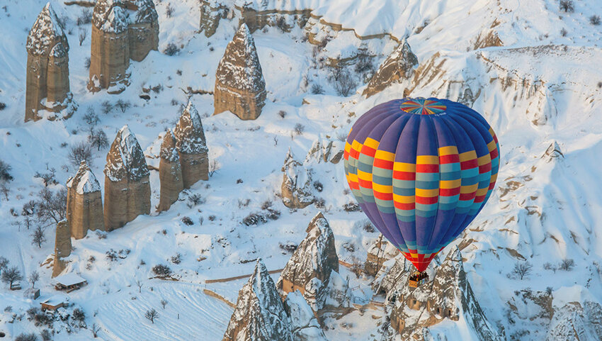 Hot air ballon over snowy landscape and fairy chimny rock formations.