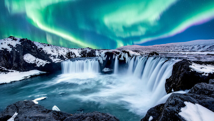 Northern lights over snow covered land and waterfall. 