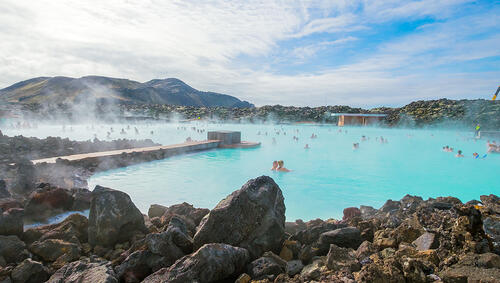 People in thermal pool with steam rising from water. 