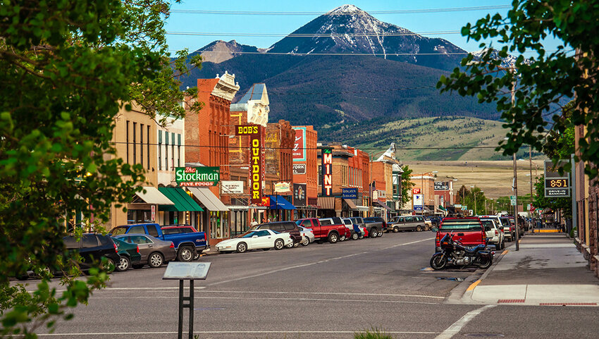 Car lined main street with snow covered mountain in background.