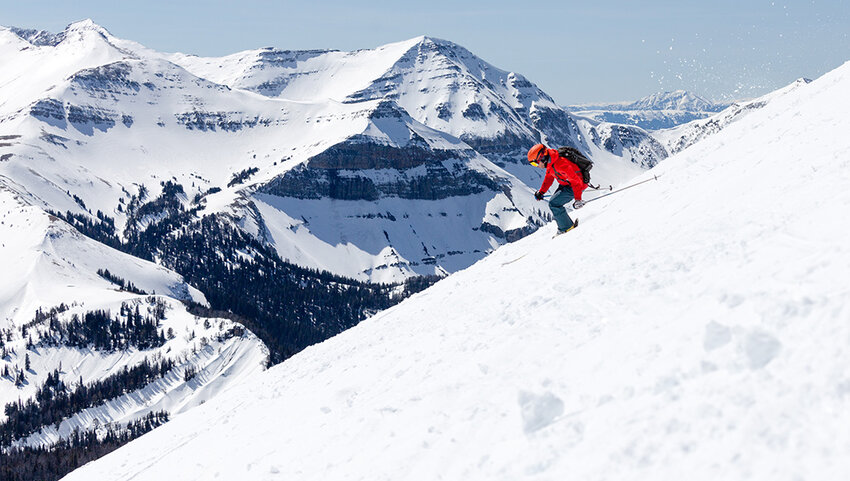 Skier going down slope with  Rocky Mountains in background.